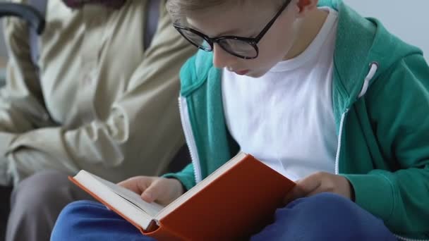 Okos fiú könyvével érdeklődéssel és nagypapa hallgat ül a kanapén — Stock videók