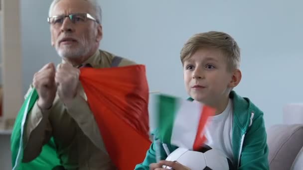 Школьник с дедушкой смотрят футбольные соревнования вместе, итальянские болельщики — стоковое видео