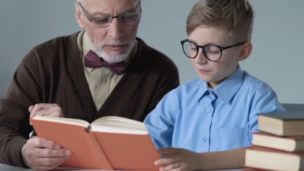 Profesor mayor leyendo libro con el alumno masculino, explicando el tema de la escuela, educación — Vídeos de Stock