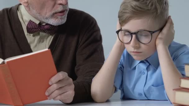 Skola pojke som täcker öronen ignorerar farfar förklara honom tråkig ämne — Stockvideo