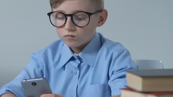 Menino da escola adorável em óculos jogando jogo de smartphone em sala de aula durante o intervalo — Vídeo de Stock