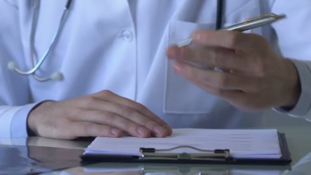 Joven doctor llenando tarjeta de paciente, anotando síntomas de enfermedad, diagnóstico — Vídeo de stock