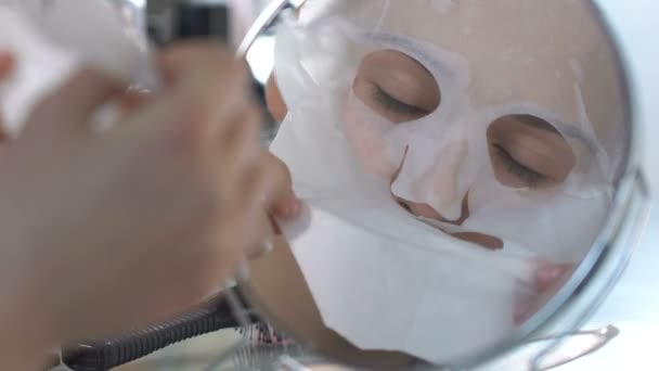 Menina bonita decolando máscara de tecido hidratante no espelho frontal, pele perfeita — Vídeo de Stock