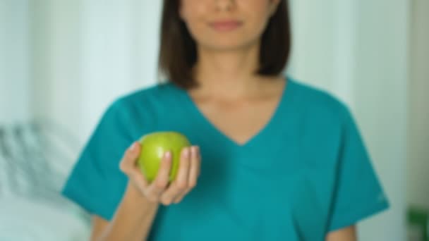 Женщина-врач предлагает зеленое яблоко, здоровый образ жизни диеты, стоматологическая помощь — стоковое видео