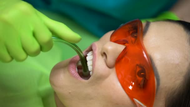 Paciente con gafas protectoras rojas esperando mientras el dentista usa el eyector de saliva — Vídeo de stock