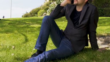 Park ve smartphone, kentsel konuşurken çimenlikte oturan iş kişi