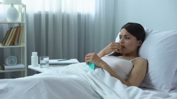 Грустная и расстроенная женщина, принимающая сильные таблетки лежа в постели, курс химиотерапии — стоковое видео