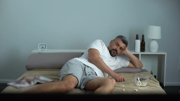 Чоловік засинає, коли їсть попкорн перед телевізором, холостяцький пасивний спосіб життя — стокове відео