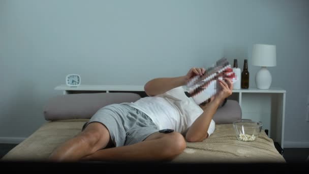 Uomo solitario entusiasticamente sfogliando rivista con contenuti per adulti sdraiato in camera da letto — Video Stock