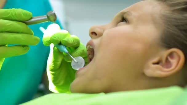 Детский дантист сверлит зуб маленькой девочке, своевременное лечение кариеса — стоковое видео