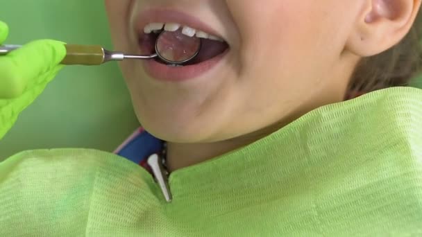 Захоплений дитина сидить у стоматологічному кріслі, лікар оглядає зуби спеціальним дзеркалом — стокове відео
