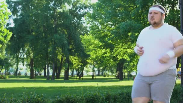 Ожирний чоловік бігає в міському парку, долаючи лінь і невпевненість, наполегливий — стокове відео