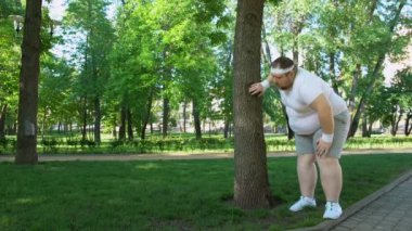 Şişman adam parkta ağaç, yorucu egzersiz programı açık havada eğilerek çalıştırdıktan sonra yorgun
