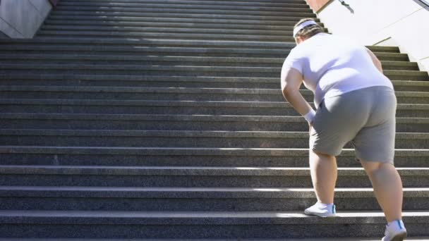 Толстяк, сидящий на лестнице после пробежки, не верящий в себя, подавленный неуверенный в себе — стоковое видео