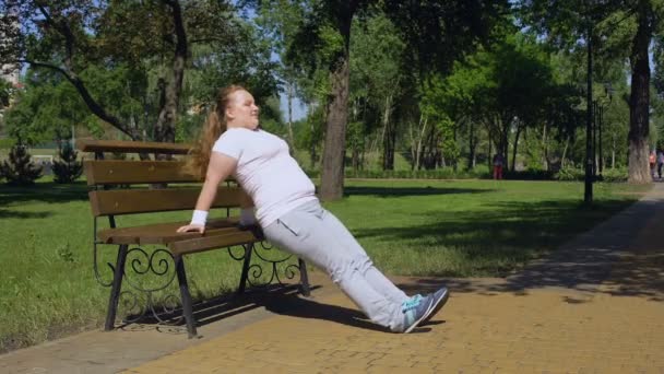 Zwaarlijvige meisje uit te oefenen op bankje in park, ijver, sport die beschikbaar zijn in elke plaats — Stockvideo