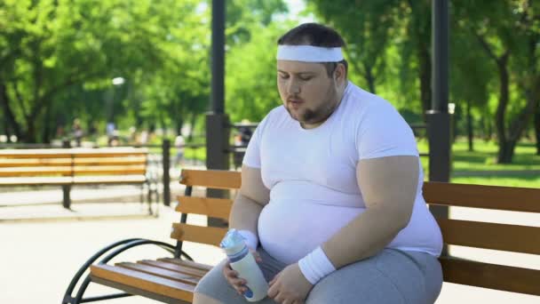 Hombre gordo respirando pesadamente y bebiendo agua después de intensos entrenamientos en el parque — Vídeo de stock