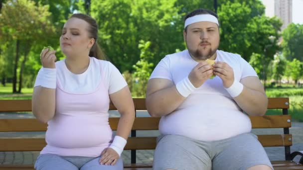 Chica gorda comiendo manzana, hombre obeso teniendo hamburguesa, elección individual de la comida adecuada — Vídeo de stock