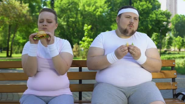 Gordura jovem casal comer hambúrgueres, viciado em junk food, falta de força de vontade — Vídeo de Stock