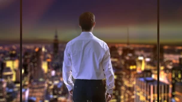 Бизнесмен поднимает руки, счастлив после хорошей сделки, рассматривая ночной город из окна — стоковое видео