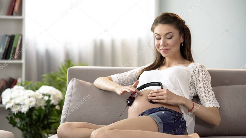 Pregnant woman holding headphones on stomach, prenatal music therapy relax
