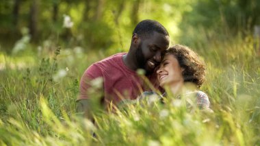 Çok ırklı çift gülüyor ve otların arasında yalan sırasında sohbet açık tarihi