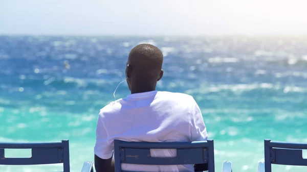 若い男性の座っていると輝く海を見て ベンチで音楽を聞く — ストック写真