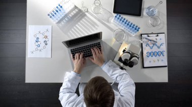 Mikroskop altında örnek ile ilgilenen gözlem dizüstü bilgisayarda yazarak araştırmacı