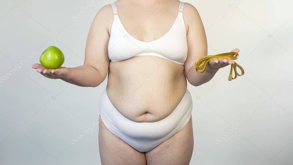Plump female holding apple and tape-line, healthy lifestyle, diet for obesity