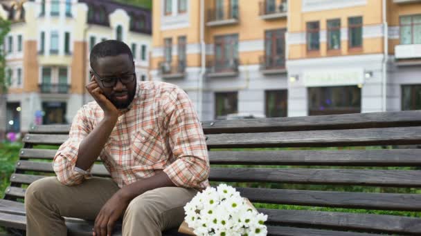 花の花束と市のベンチに孤独な坐っている悲しいアフリカ人失敗した日付 — ストック動画