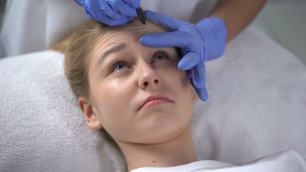 Kosmetikerin markiert tiefe Stirnfalten im Gesicht der Klienten, Schönheitsoperationen