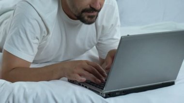 Adam yatakta yatan ve başparmak yukarıya, serbest meslek sahibi çevrimiçi çalışmaya gösterilen laptop yazarak