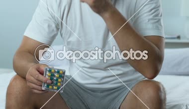 Hapları blister, mens sağlık sorunu tutan yatağın üstüne oturan üzgün yakışıklı adam