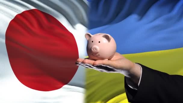 Japan Investment Ukraine Hand Putting Money Piggybank Flag Background — Stock Video