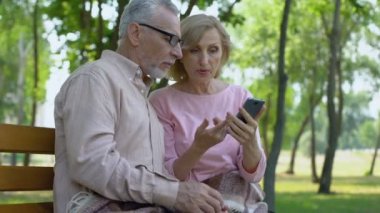 Eşi kullanma smartphone, kıdemli mutlu çift birlikte parkta yaşlı adam yardım yaşlı