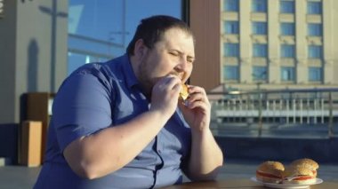Şişman adam ısırma lokanta hamburger, akşam yemeğinde açık kafe, böylece aşırı yeme sorunu