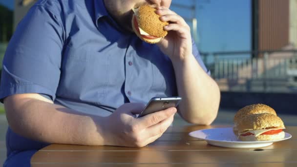 Luie Jonge Man Ongezonde Hamburger Eten Schuiven Smartphone Applicatie — Stockvideo