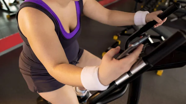 Fitness Application Obese Girl Riding Exercise Bike Scrolling Mobile Gadget — Stock Photo, Image