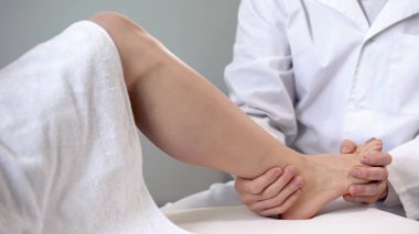 Traumatologist moving patient ankle, assessing severity of injury, closeup clipart