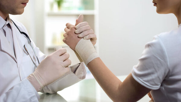 Male physician bandaging females sprained wrist, first aid in hospital, medicine