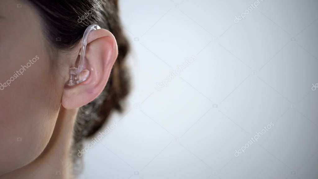 Closeup of ear with hearing aid, young deaf woman adjusting to environment