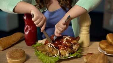 Obese teenager girl carving greasy chicken covered with ketchup and mayonnaise clipart