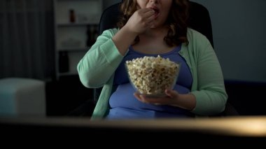 Chubby woman taking handful of popcorn and eating in front of TV, laziness clipart