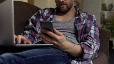 Adam kanepede oturan ve laptop, smartphone, iş başvurusu kaydırma yazarak