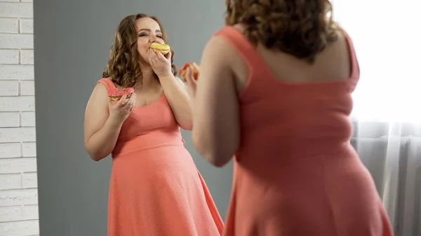 快乐肥胖夫人满意她的身体吃甜甜圈在镜子前 — 图库照片