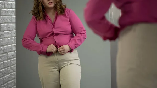 Obese lady buttoning up tight shirt on stomach with effort, overweight problem