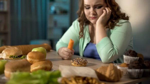 ドーナツ ファーストフード 健康的な食事を夢見て ニンジンを食べて空腹の太った女性 — ストック写真