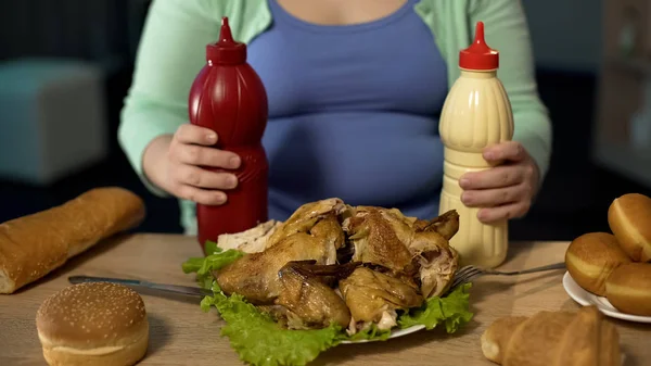 胖女士拿着番茄酱和蛋黄酱的瓶子 准备吃烤鸡肉 — 图库照片