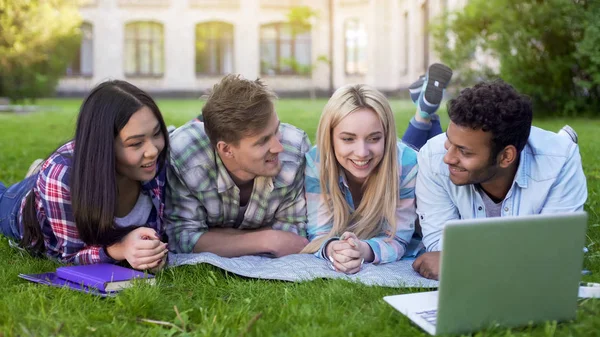Multiracial friends watching and laughing at video on laptop, students at break