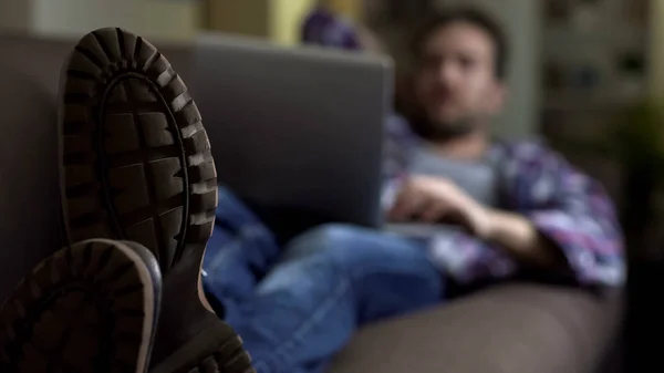 男のブーツでソファの上に横たわるとラップトップ 社会のウェブサイト 通信を使用して — ストック写真