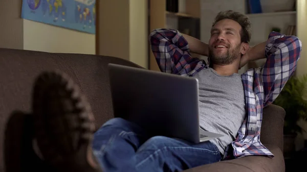 Удовлетворенный Мужчина Лежит Диване Ноутбуком Улыбаясь Наслаждаясь Отдыхом Дома — стоковое фото